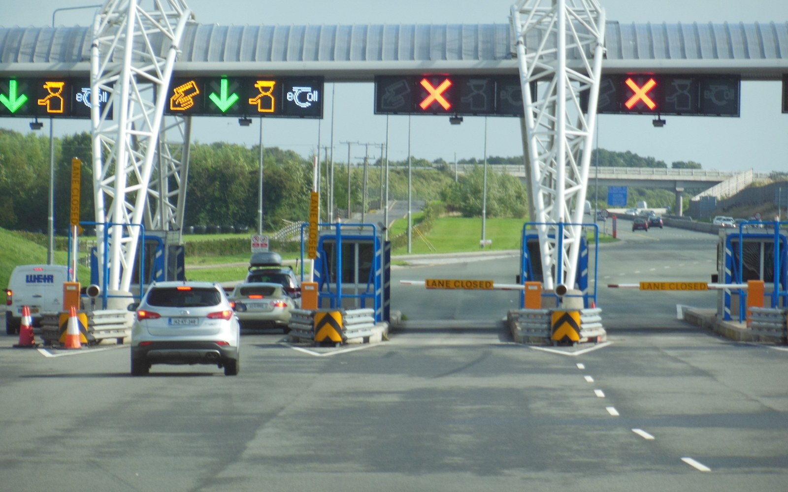 A queue of cars at a toll plaza in flat daylight